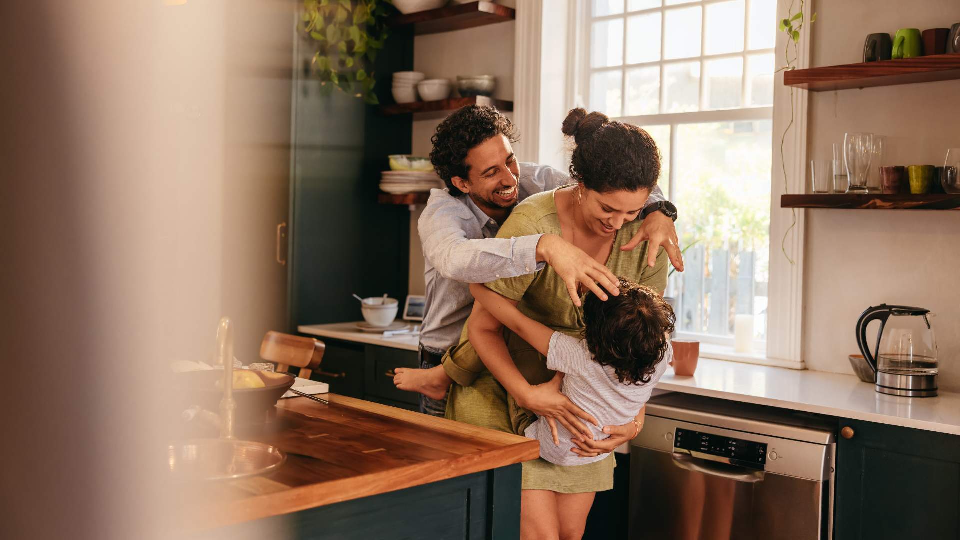 A man and woman hugging their child in a rustic warm kitchen.