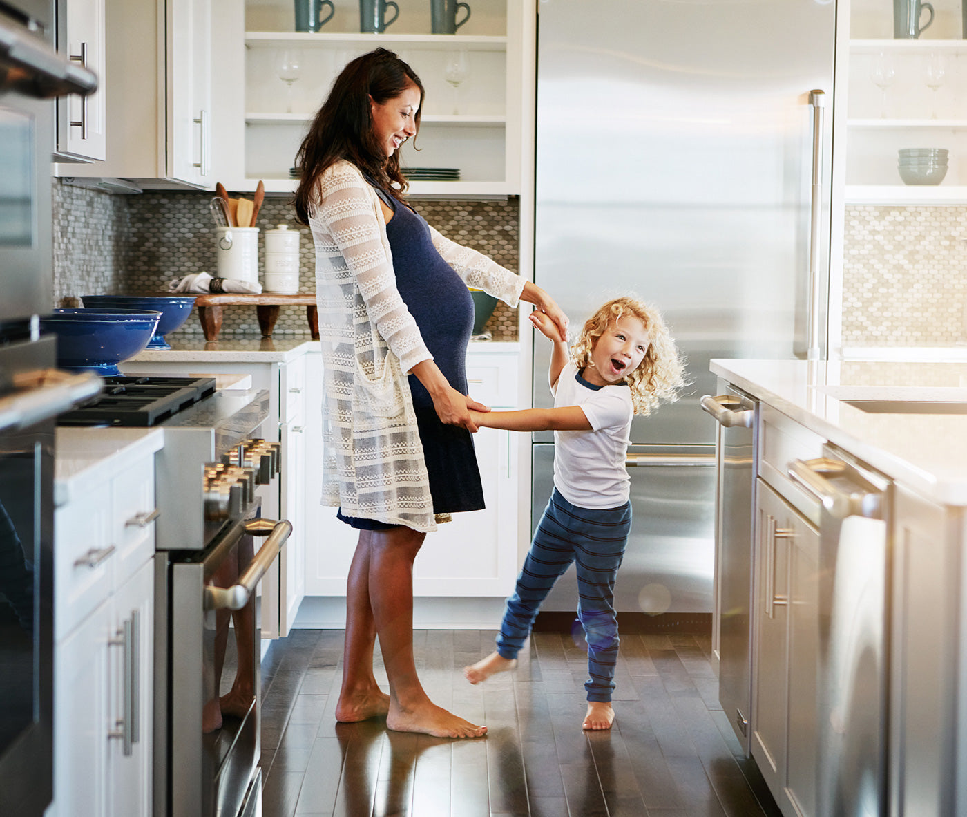 Pregnant woman and child dancing together in a modern kitchen