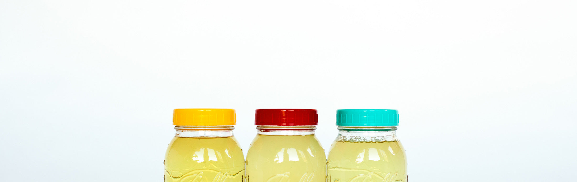 Three bottles with colorful lids filled with liquid soaps against a white background