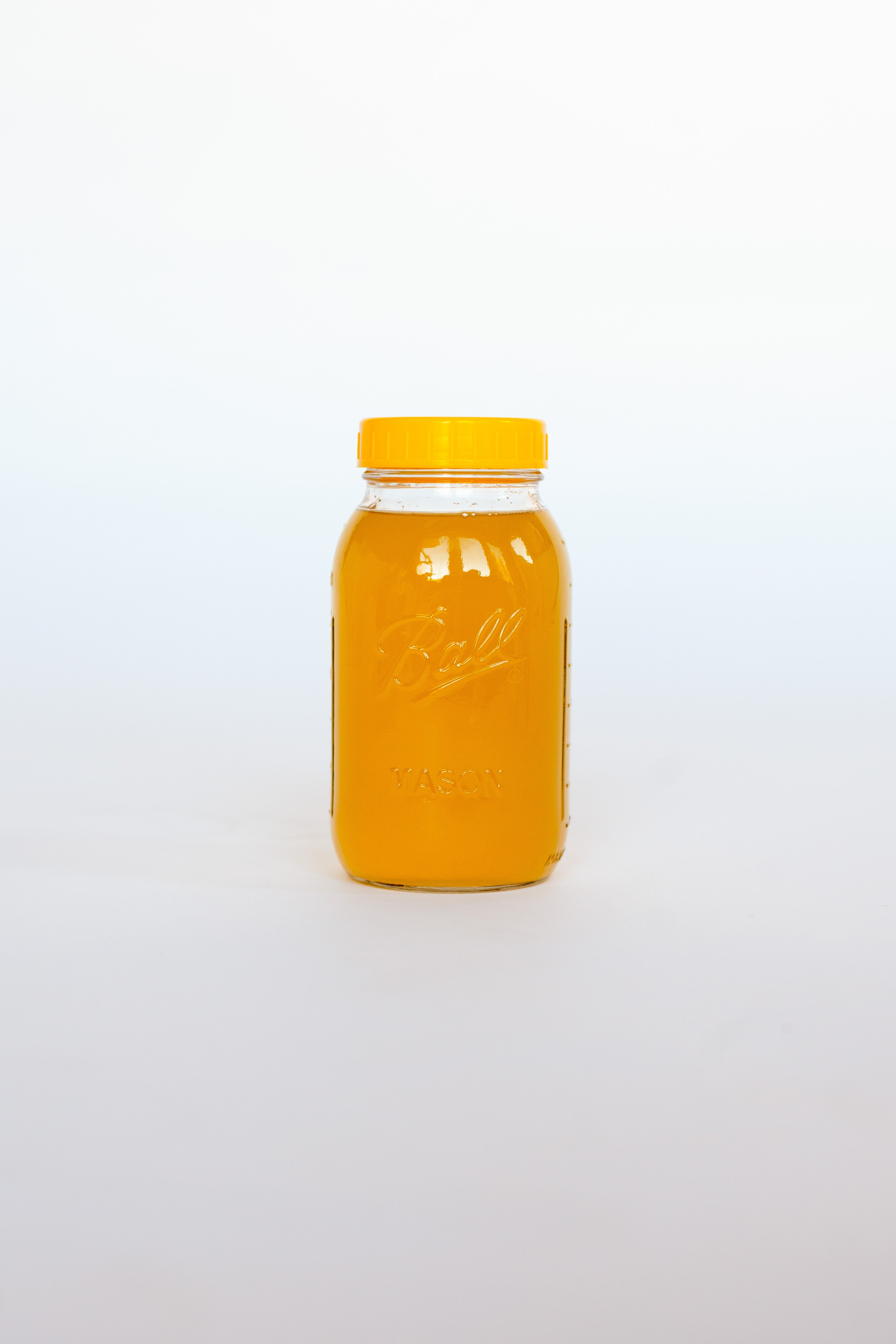 Clear glass jar with a yellow lid containing an orange liquid soap on a white background