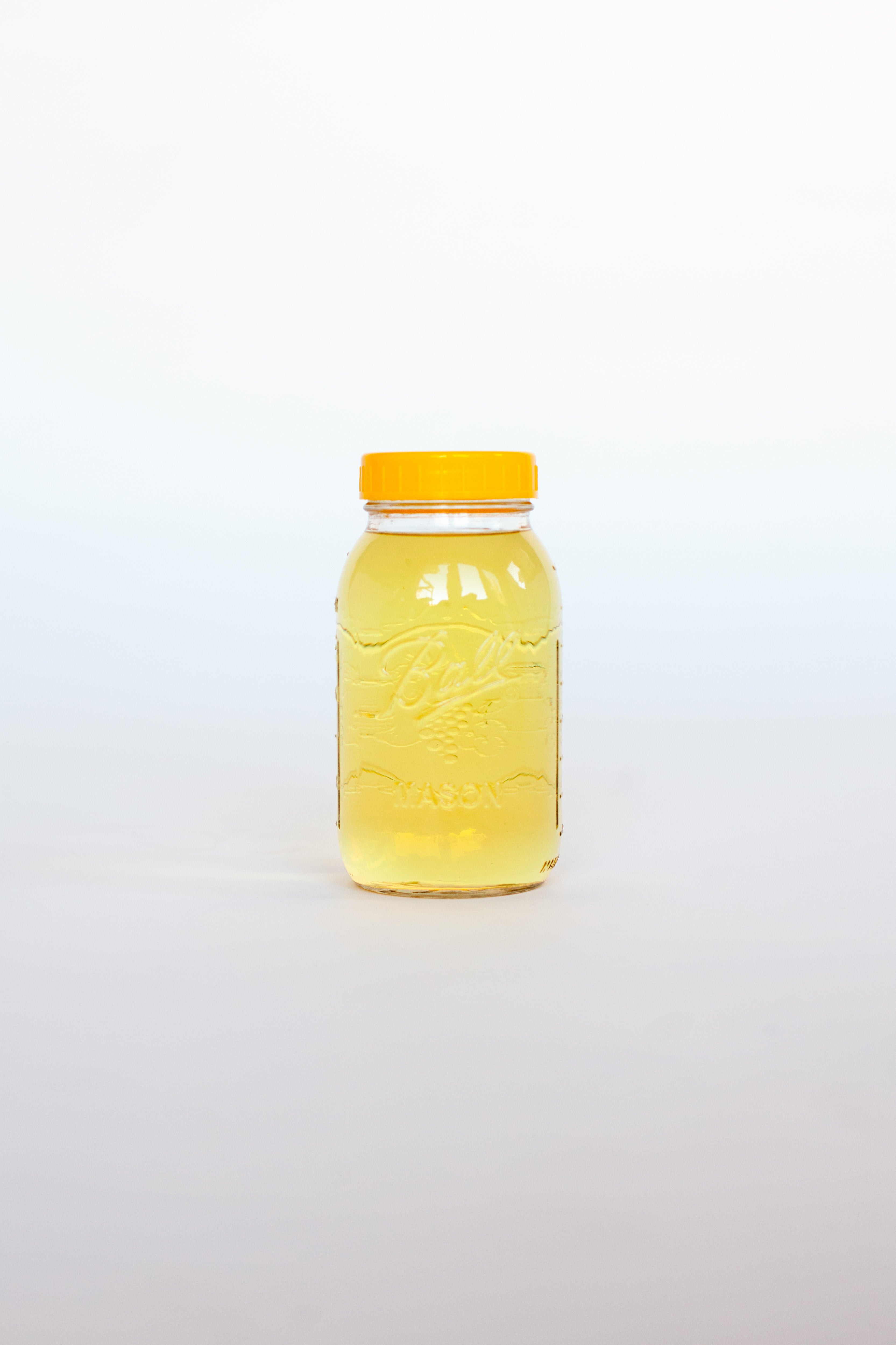 Clear glass jar with a yellow lid containing a yellow liquid soap on a white background