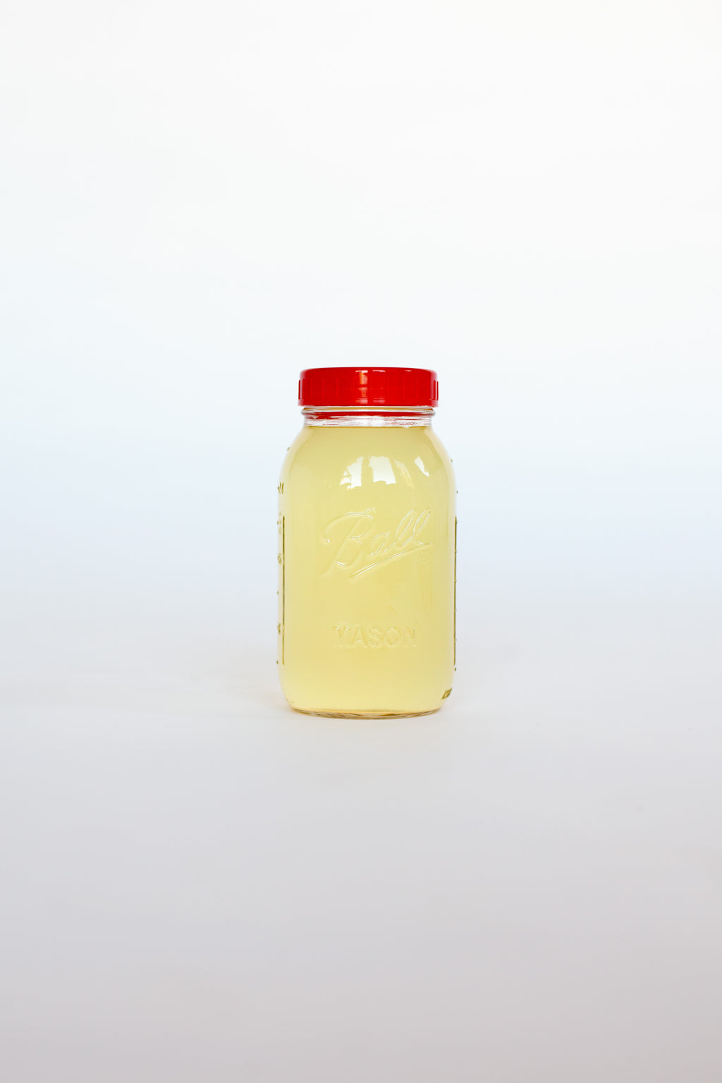 Clear glass jar with a red lid containing a yellow liquid soap on a white background