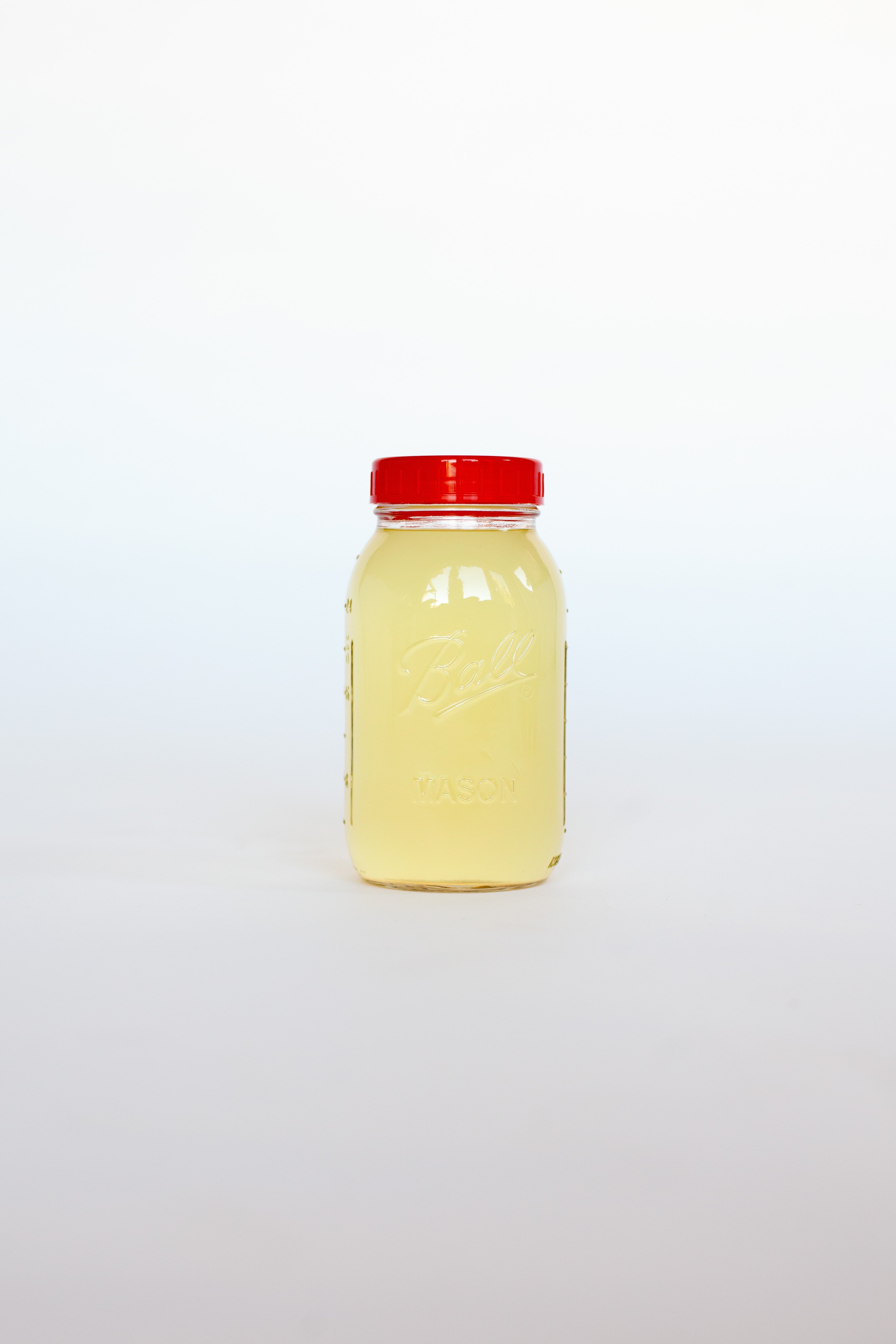Clear glass jar with a red lid containing a yellow liquid soap on a white background