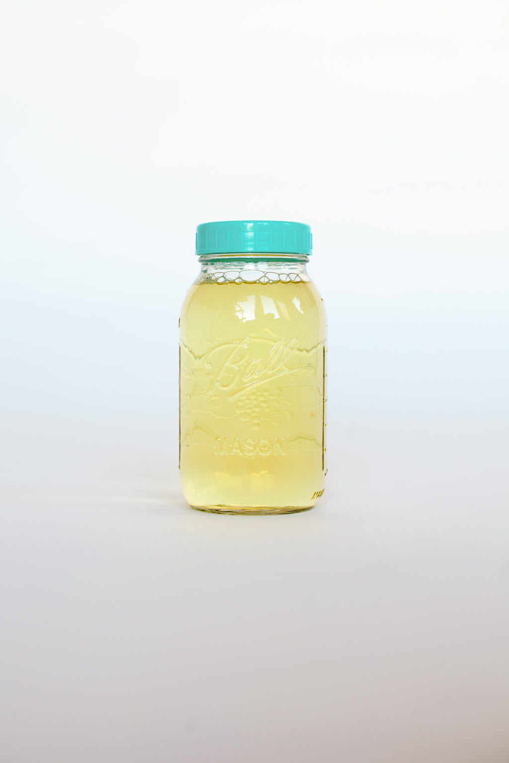 Clear glass jar with a green lid containing a yellow liquid soap on a white background